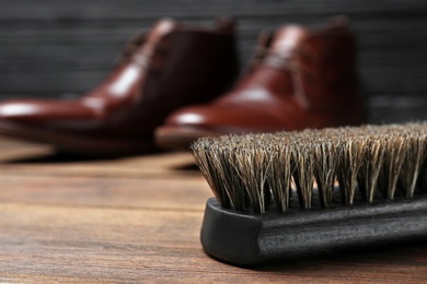Photo of Shoe brush and leather footwear on wooden surface, space for text