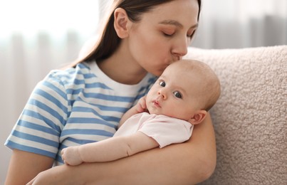 Photo of Mother kissing her cute baby in armchair at home