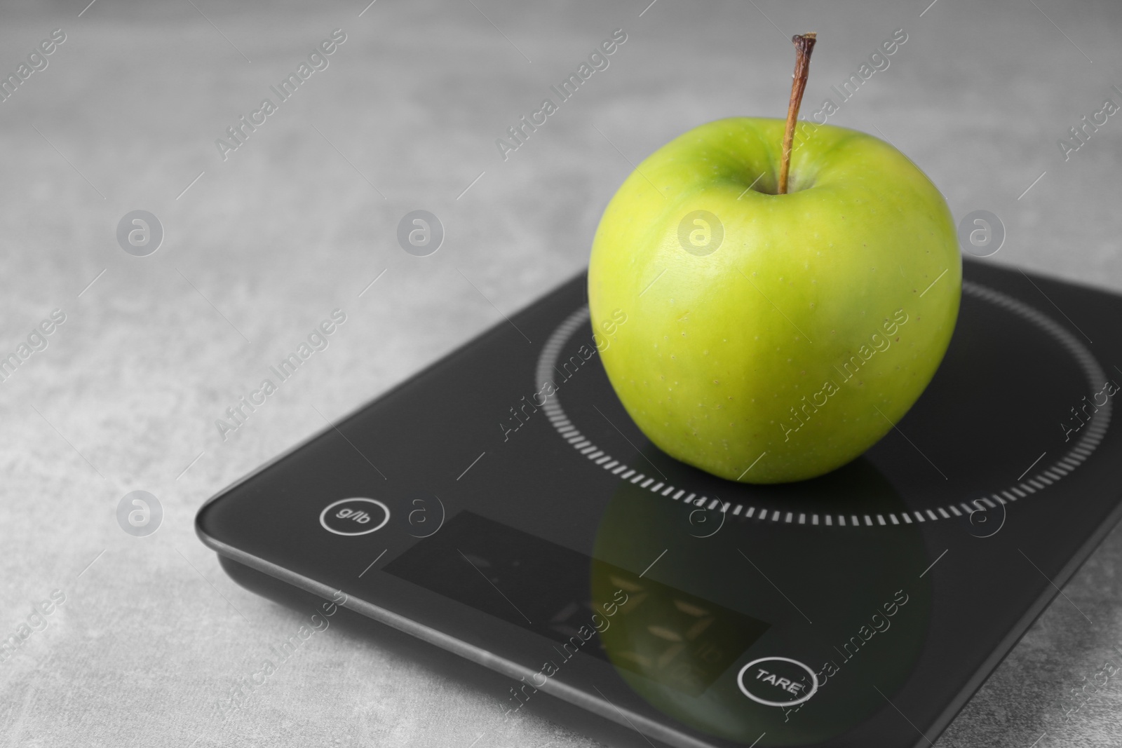 Photo of Digital kitchen scale with ripe green apple on grey table, closeup