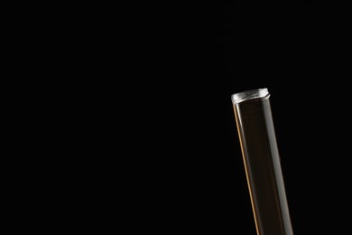 Photo of Test tube with brown liquid on black background, closeup. Space for text