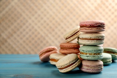 Photo of Delicious macarons on light blue wooden table. Space for text