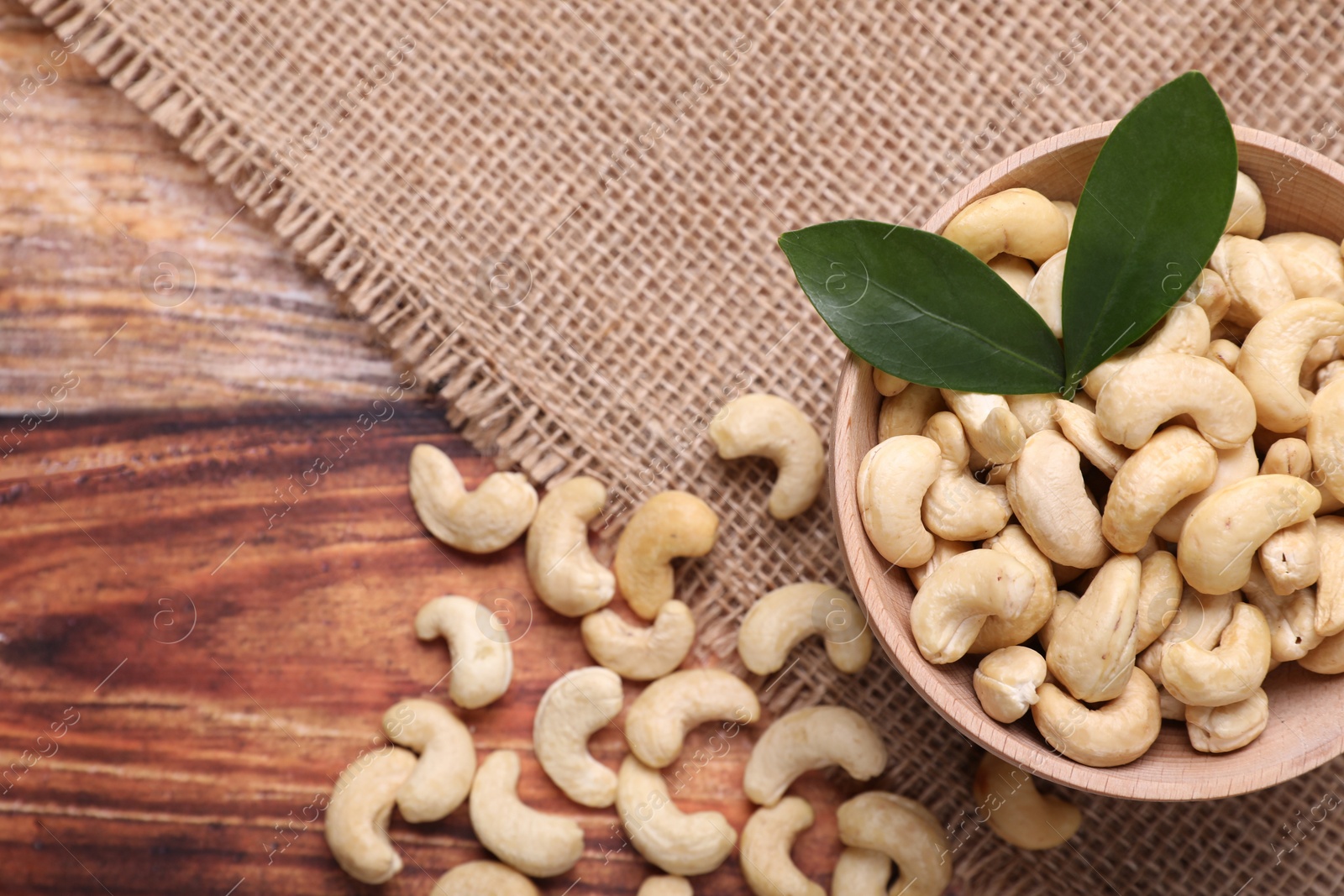 Photo of Tasty cashew nuts and green leaves on wooden table, top view