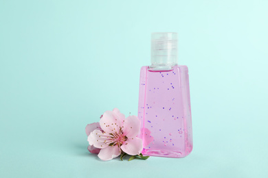 Photo of Bottle with antiseptic gel and flowers on light blue background
