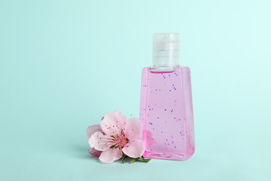 Bottle with antiseptic gel and flowers on light blue background