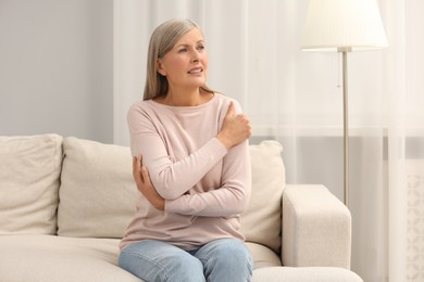 Photo of Mature woman suffering from pain in arm on sofa at home. Rheumatism symptom