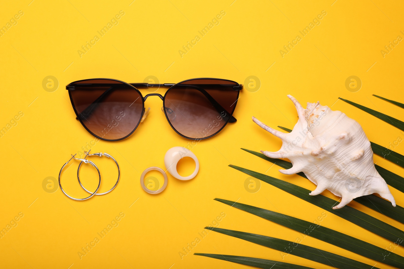 Photo of Flat lay composition with stylish sunglasses, seashell and accessories on yellow background