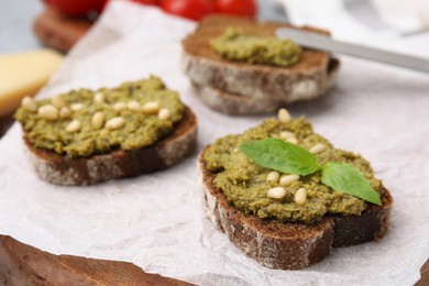 Photo of Tasty bruschettas with pesto sauce, nuts and fresh basil on wooden board, closeup