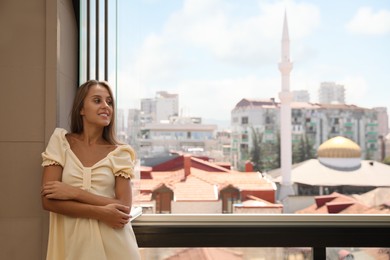 Photo of Beautiful young woman standing on balcony, space for text