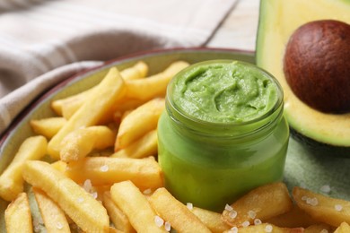 Plate with french fries, guacamole dip and avocado served on white wooden table, closeup
