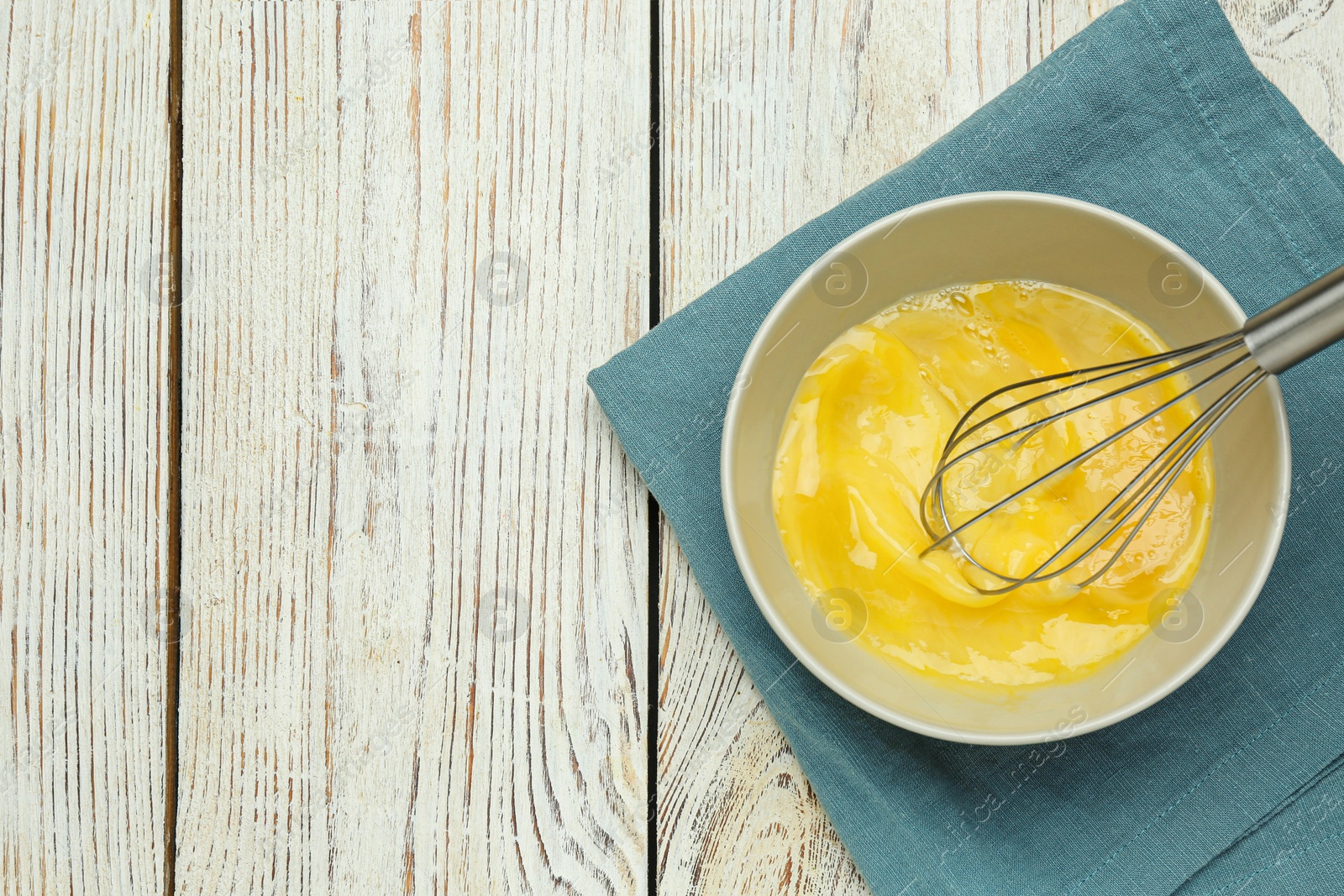 Photo of Whisking eggs in bowl on wooden table, top view. Space for text