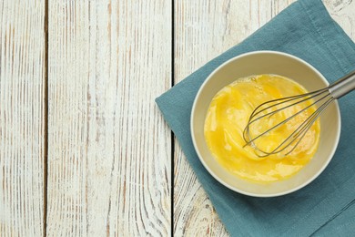 Whisking eggs in bowl on wooden table, top view. Space for text