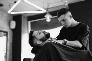 Image of Professional hairdresser working with bearded client in barbershop. Black and white effect