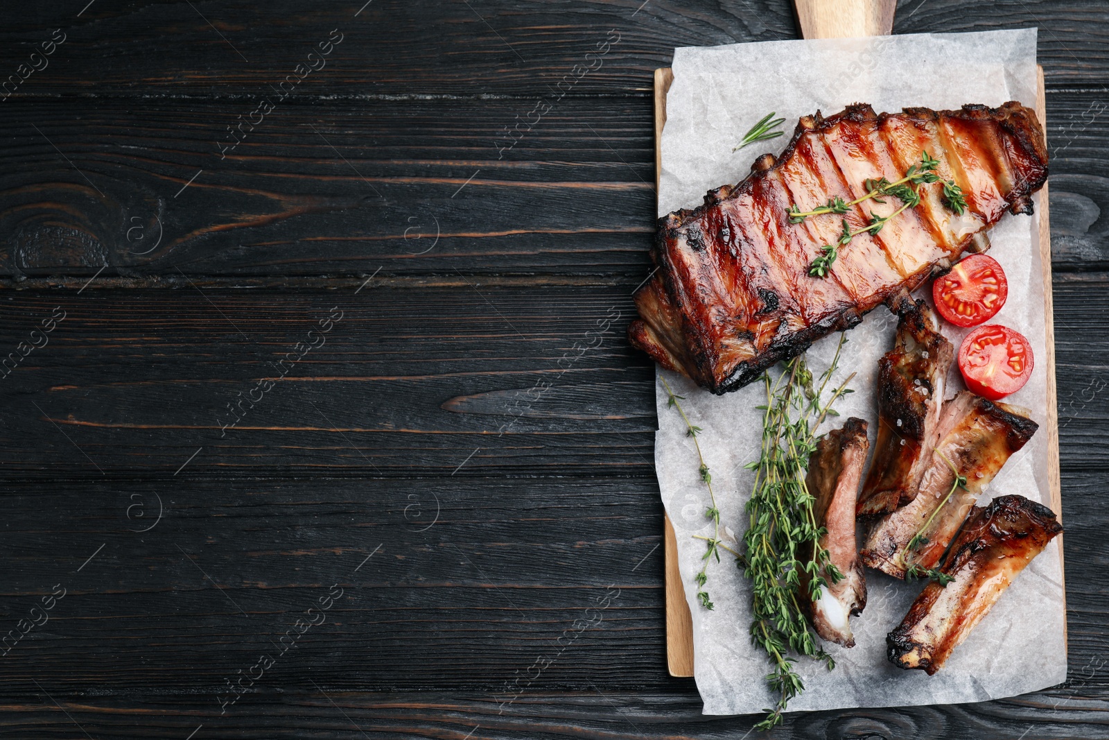 Photo of Tasty grilled ribs on black wooden table, flat lay. Space for text