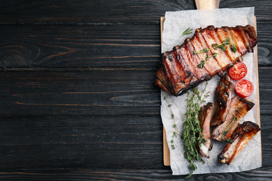 Photo of Tasty grilled ribs on black wooden table, flat lay. Space for text