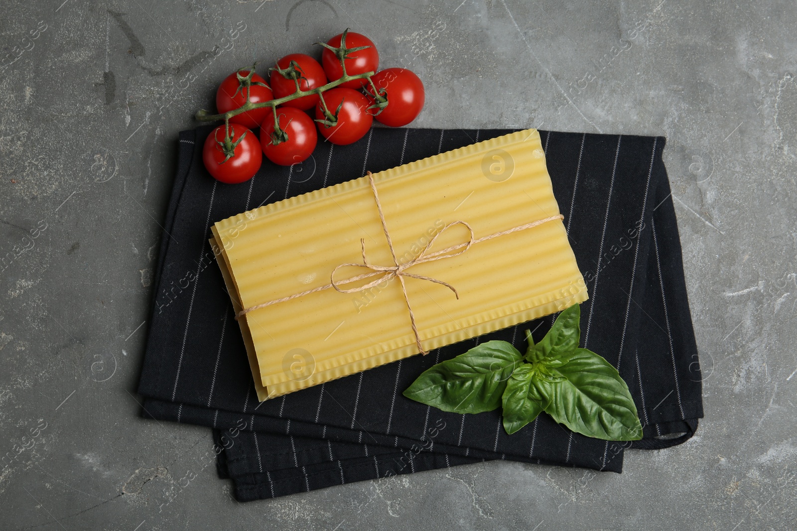 Photo of Uncooked lasagna sheets, cherry tomatoes and basil on grey table, flat lay