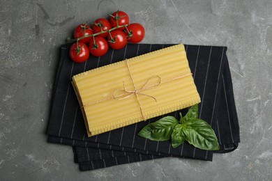 Photo of Uncooked lasagna sheets, cherry tomatoes and basil on grey table, flat lay
