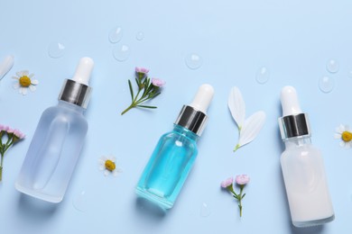 Bottles of cosmetic serums, flowers and petals on light blue background, flat lay