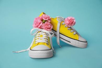 Photo of Pair of yellow classic old school sneakers and flowers on light blue background