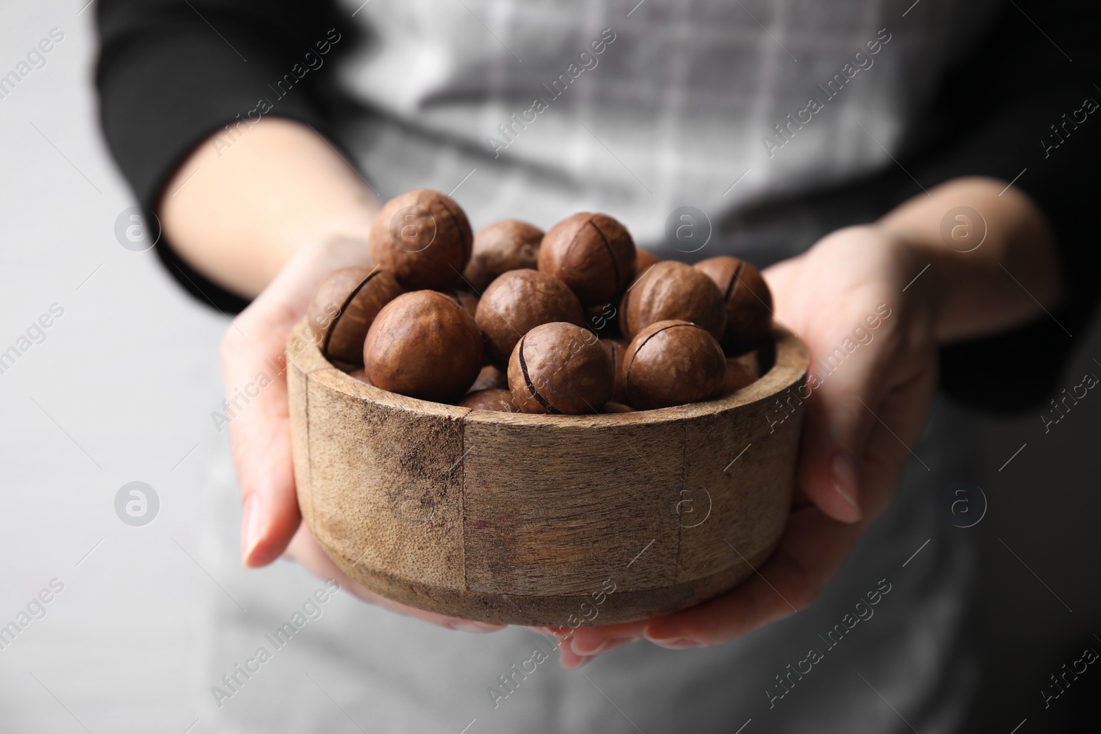 Photo of Woman holding bowl with delicious macadamia nuts, closeup