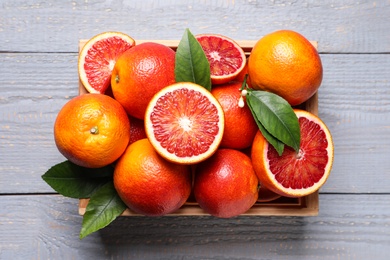 Crate of ripe red oranges and green leaves on grey wooden table, top view