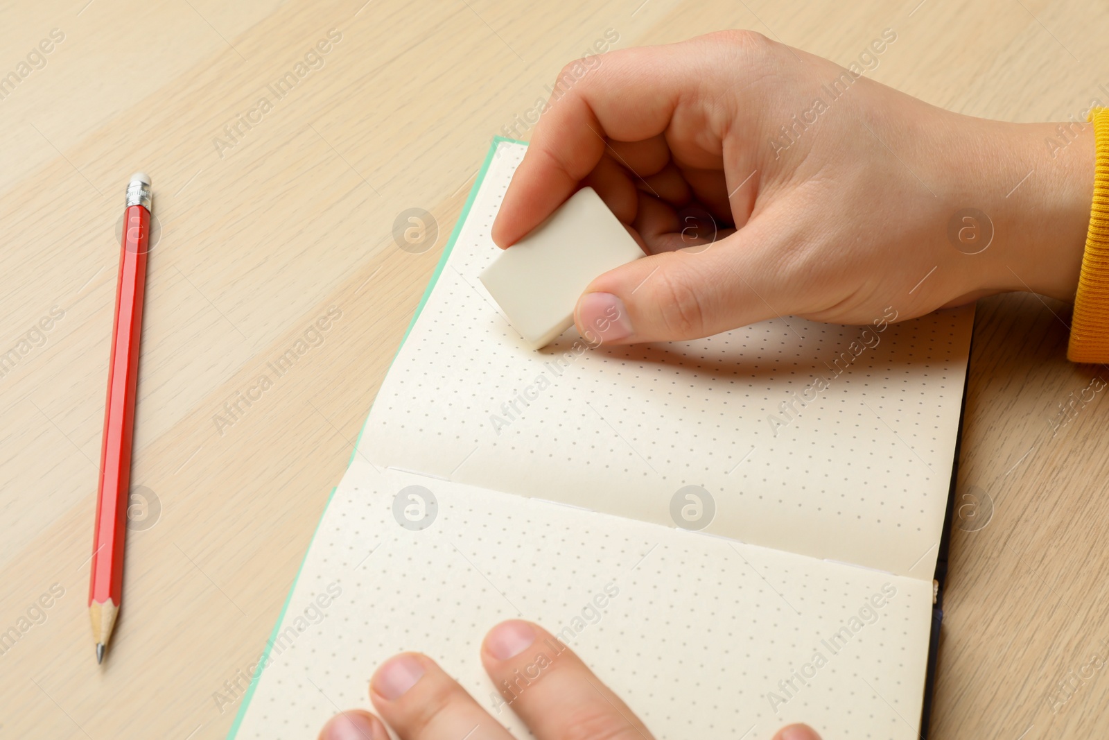 Photo of Man erasing something in notebook at wooden table, closeup