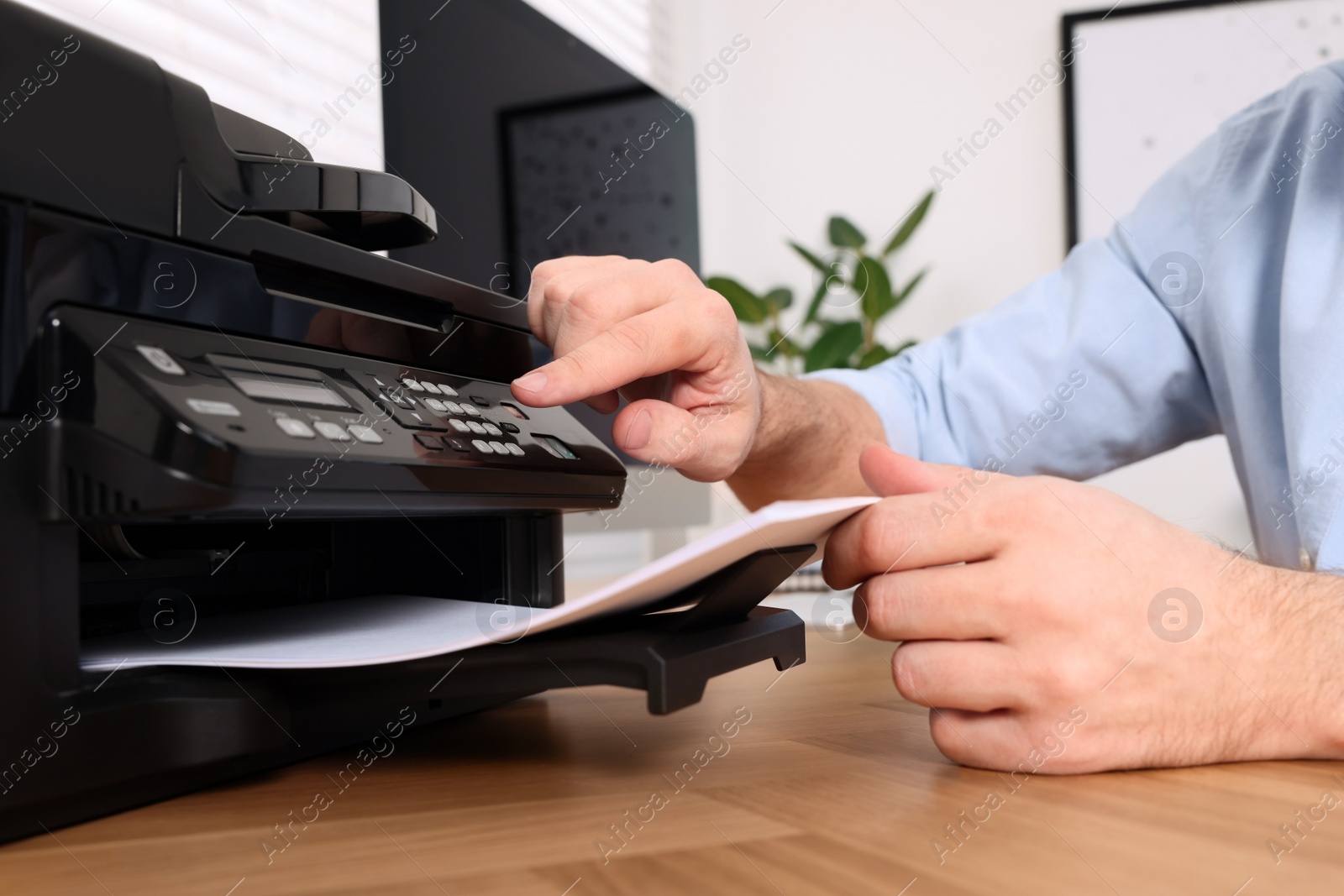 Photo of Man using modern printer at wooden table indoors, closeup