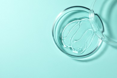 Photo of Petri dish with liquid and lid on turquoise background, top view. Space for text