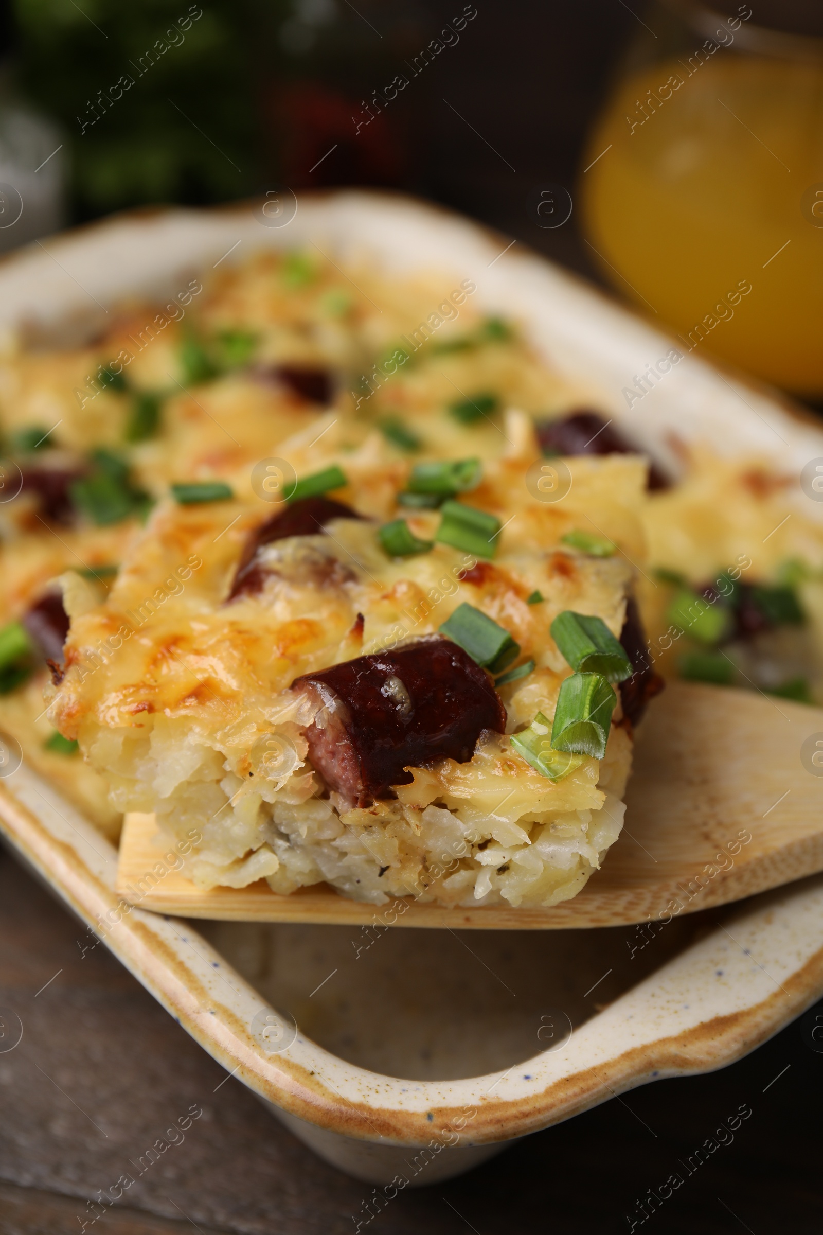 Photo of Taking piece of tasty sausage casserole from baking dish at table, closeup