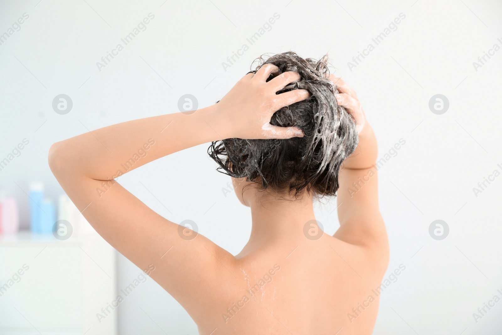 Photo of Woman applying shampoo onto her hair in light bathroom