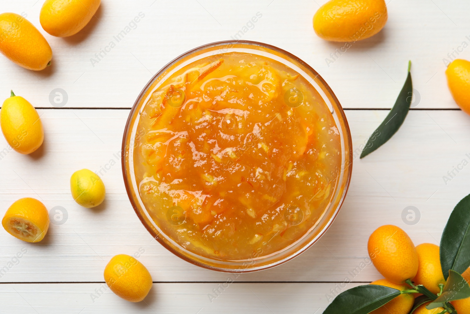 Photo of Delicious kumquat jam in bowl and fresh fruits on white wooden table, flat lay