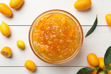 Delicious kumquat jam in bowl and fresh fruits on white wooden table, flat lay