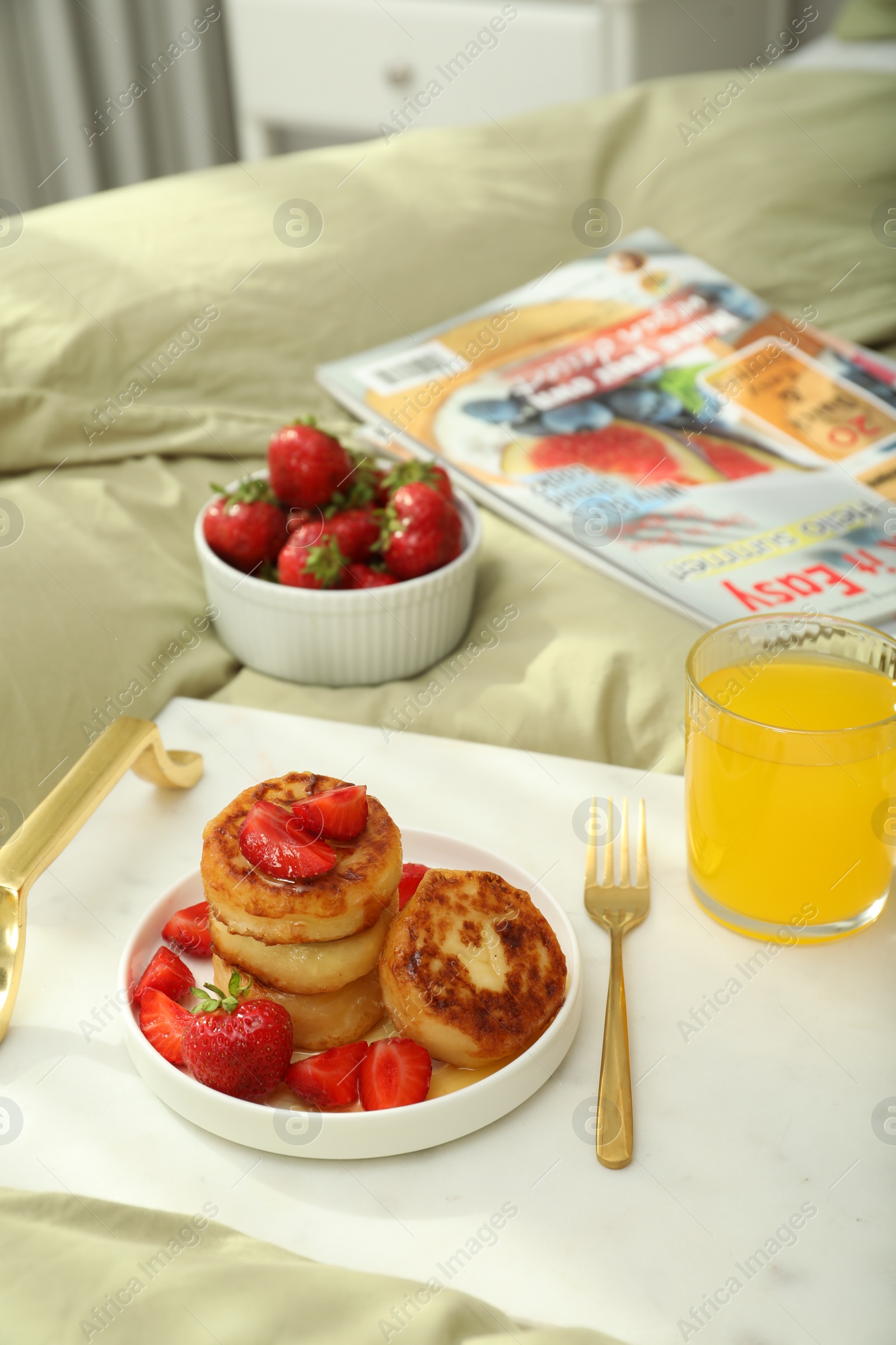 Photo of Tasty breakfast served in bedroom. Cottage cheese pancakes with strawberries and honey on white tray