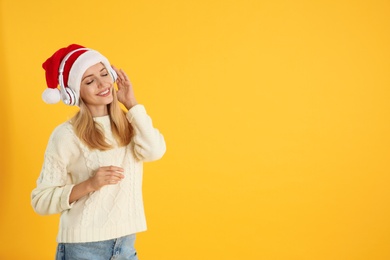 Photo of Happy woman with headphones on yellow background, space for text. Christmas music