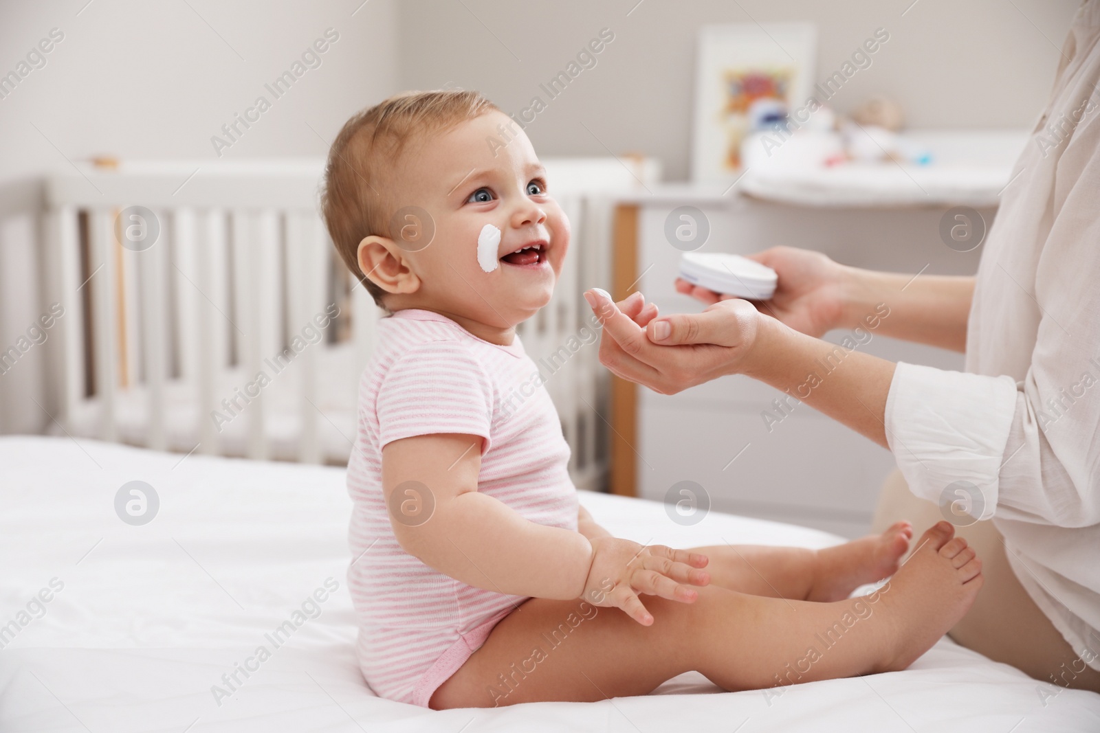 Photo of Mother applying moisturizing cream on her little baby at home, closeup