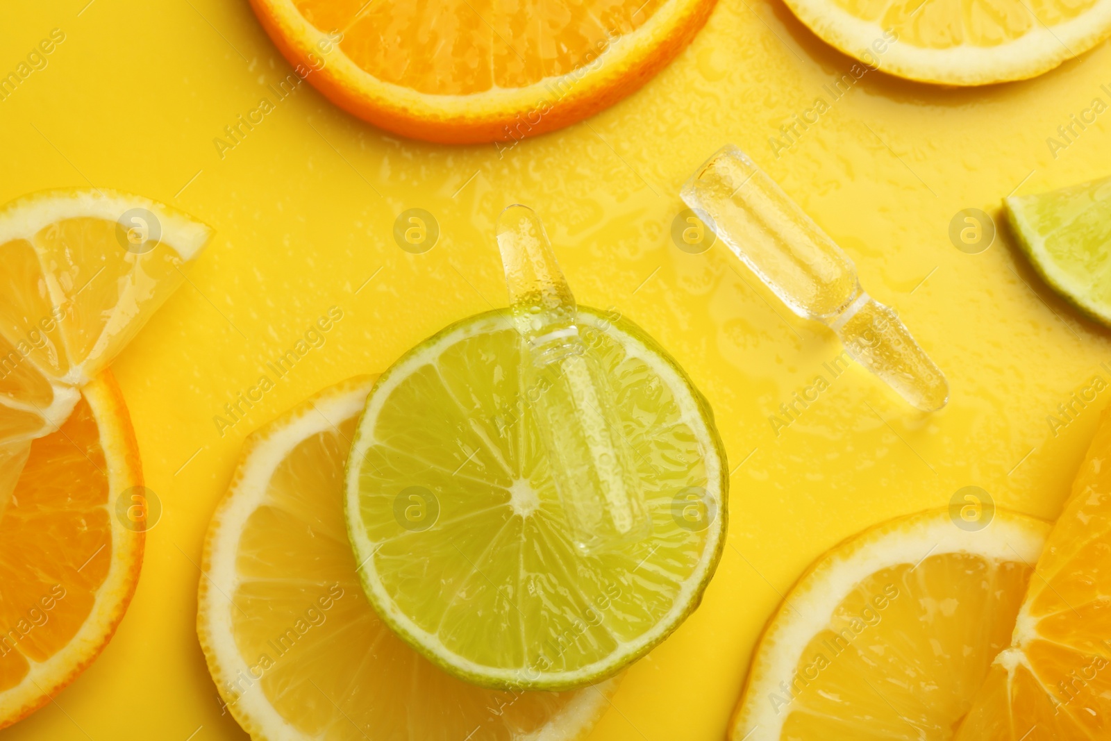 Photo of Skincare ampoules with vitamin C and citrus slices on yellow background, flat lay