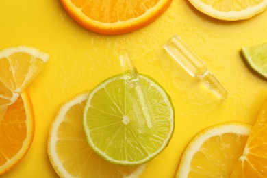 Skincare ampoules with vitamin C and citrus slices on yellow background, flat lay