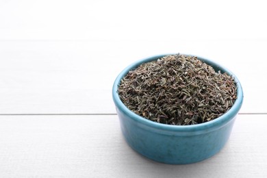 Ceramic bowl with dried thyme on white wooden table, closeup. Space for text