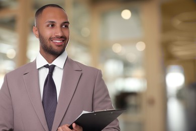 Lawyer, consultant, business owner. Confident man with clipboard smiling indoors, space for text