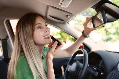 Photo of Beautiful careless woman applying makeup in car