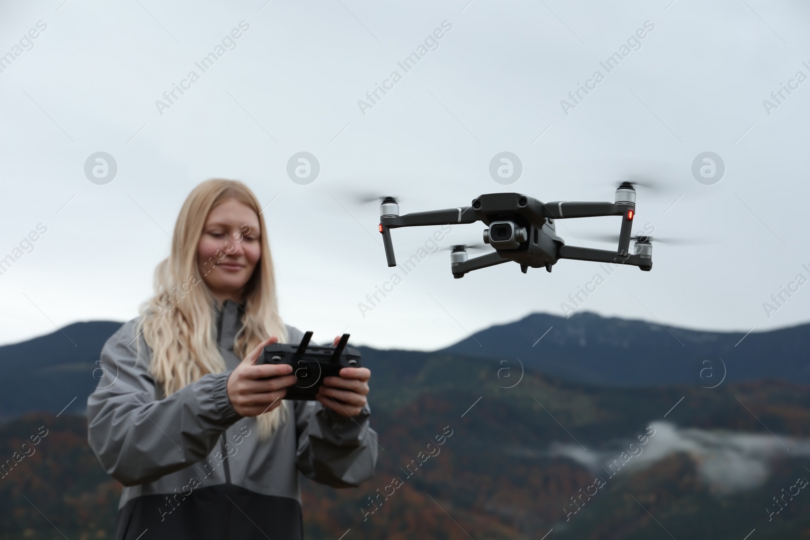 Photo of Young woman operating modern drone with remote control in mountains