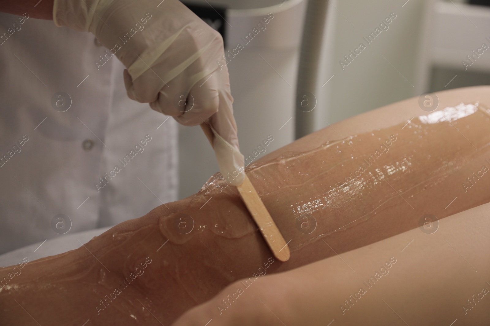 Photo of Professional cosmetologist applying gel on client's leg before laser epilation procedure in salon, closeup