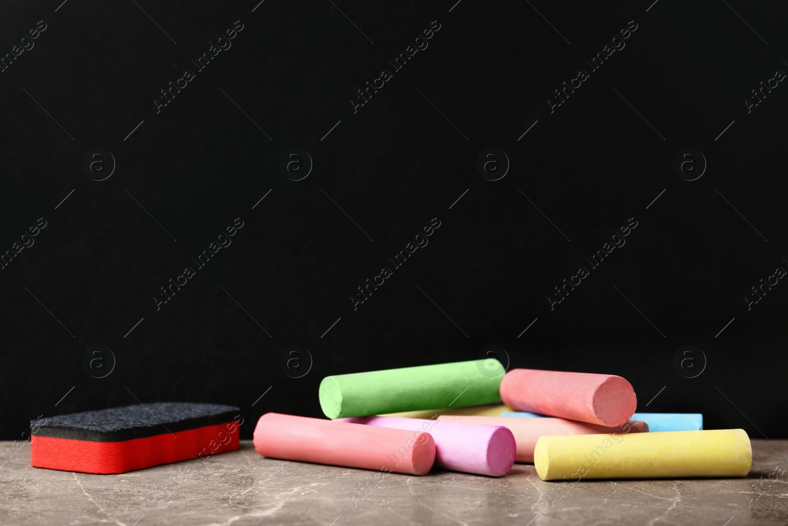 Photo of Color pieces of chalk and duster on table near blackboard
