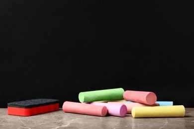 Photo of Color pieces of chalk and duster on table near blackboard