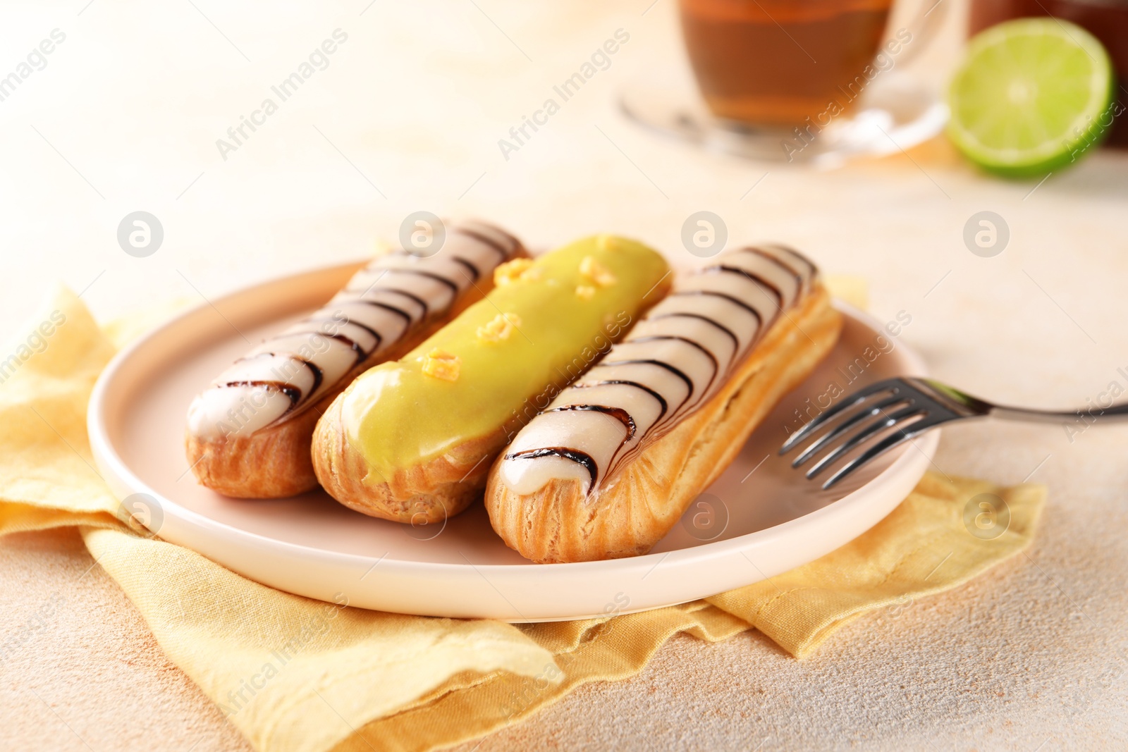 Photo of Different tasty glazed eclairs served on color textured table, closeup