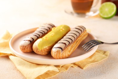 Photo of Different tasty glazed eclairs served on color textured table, closeup