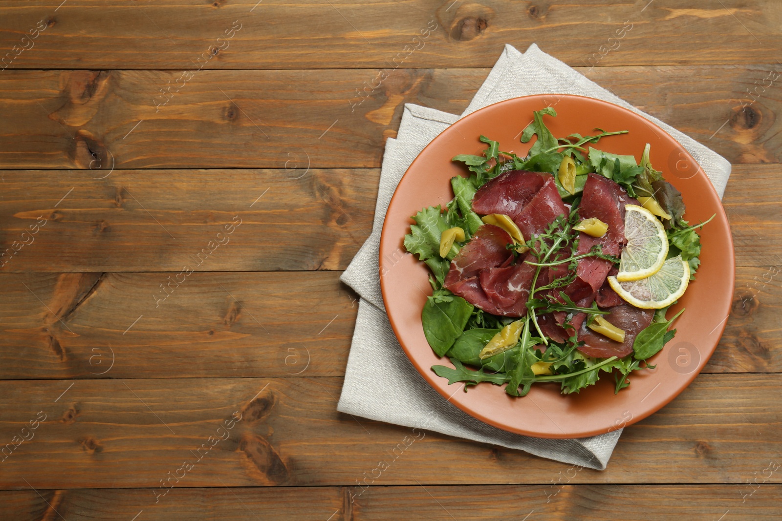 Photo of Delicious bresaola salad on wooden table, top view. Space for text