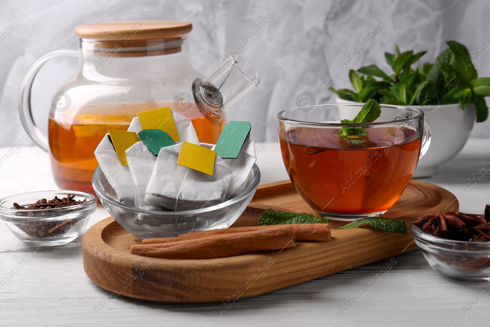 Photo of Tea bags, cup of hot drink and ingredients on white wooden table