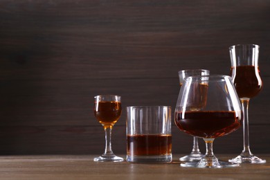 Photo of Different delicious liqueurs in glasses on wooden table. Space for text
