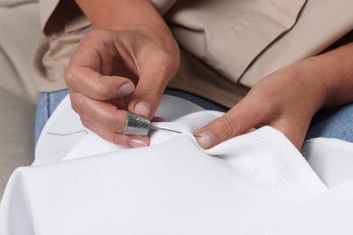 Photo of Woman embroidering on white fabric with thimble and sewing needle, closeup