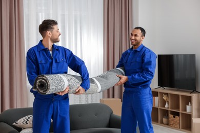 Male movers carrying carpet in new house